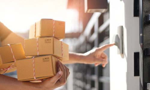 istockphoto-1182778655-612x612 Delivery man holding parcel boxes and ring the doorbell on the client's door in the morning background.