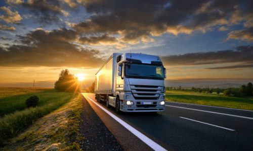 Truck driving on the asphalt road in rural landscape at sunset with dark clouds Truck driving on the asphalt road in rural landscape at sunset with dark clouds
